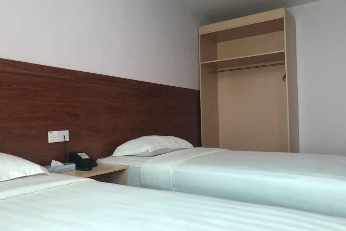 A hotel room with three beds, a wooden headboard, a wardrobe, and a bedside telephone.