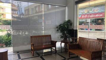 A waiting area with a checkered floor, wooden benches, and a large window with a view of a building and a sign reading 'R&H Collection'.