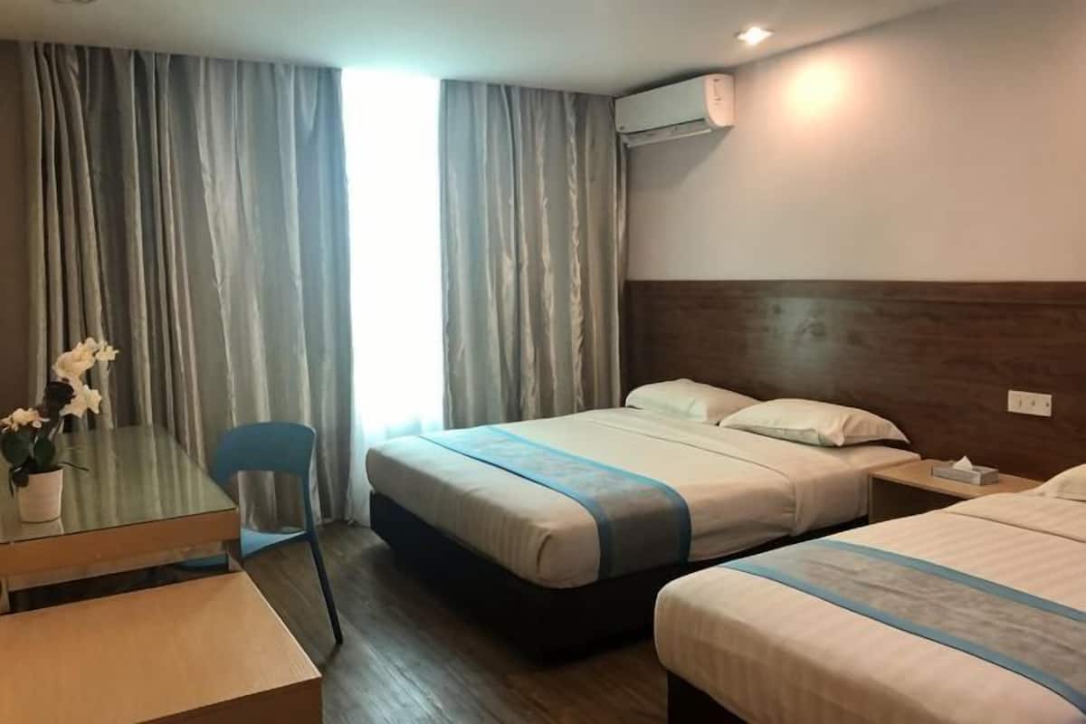 A hotel room with two beds, a desk with a chair, a small table with a vase of flowers, and a window with curtains.