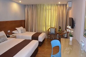 A hotel room with two beds, a desk, a chair, a TV, and a window with curtains.