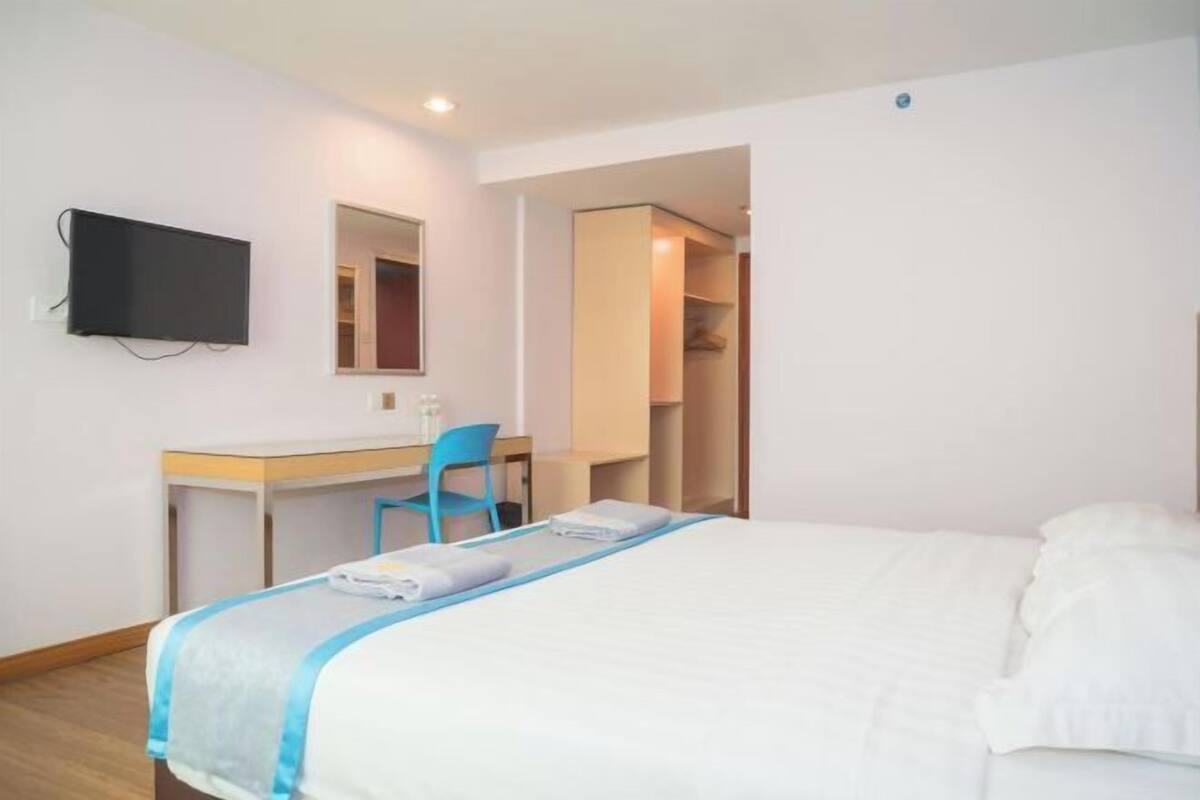 A hotel room with a bed, a desk, a chair, a television, and a wardrobe.