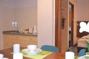 A dining area with a table set for two, a kitchen area with a sink and cabinets, and a staircase leading to another room.