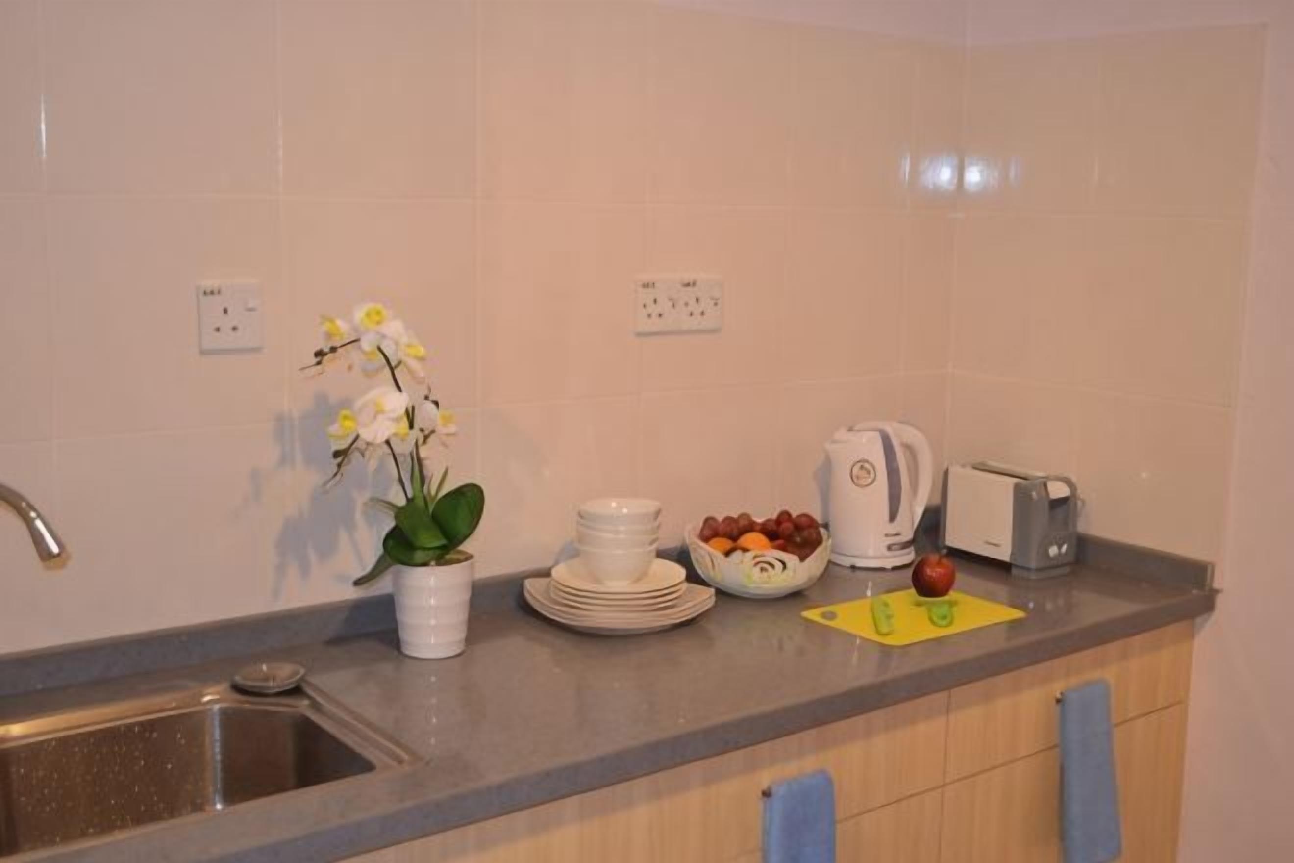 Een keuken met een spoelbak, witte tegels, een vaas met bloemen, een schaal fruit en een broodrooster.