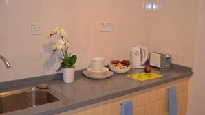A kitchen with a sink, white tiles, a vase with flowers, a bowl of fruit, and a toaster.