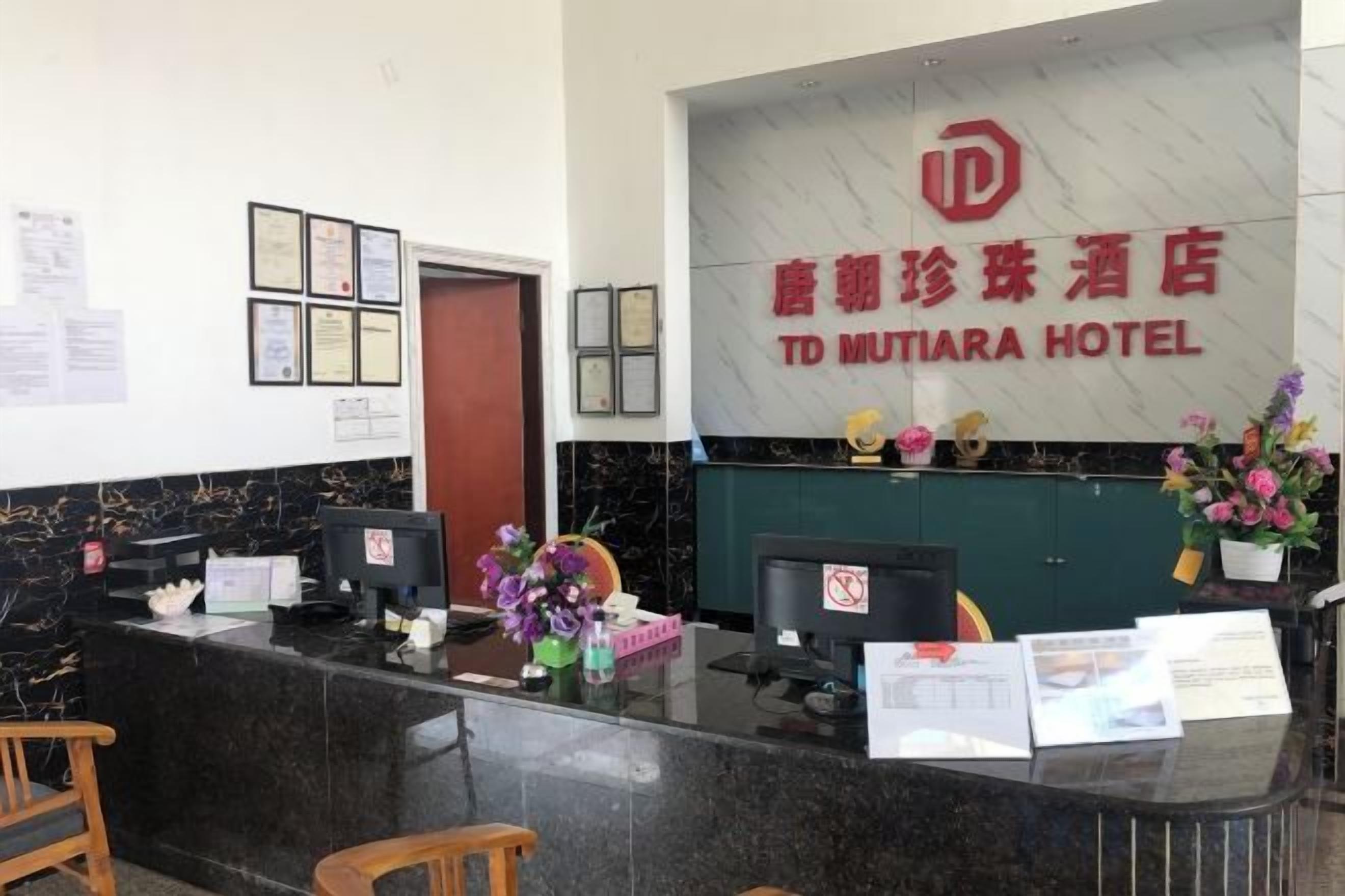 A hotel reception desk with a marble counter, framed certificates, and a sign for TD MUTIARA HOTEL.