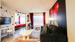 Una sala de estar moderna con un sofá, una mesa de centro, un televisor y un cuadro de Mickey Mouse rojo en la pared.