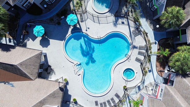 Vista aérea de una piscina con diseño en forma de corazón, rodeada de sillas de descanso y sombrillas.