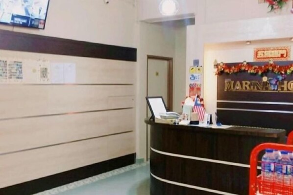 A reception desk with a computer and a telephone, a wall with papers, and a sign above the desk. - Marina Hotel Kemaman (Chukai)