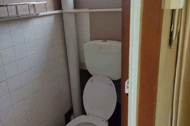 A small bathroom with a toilet, a white tiled wall, and a beige door.