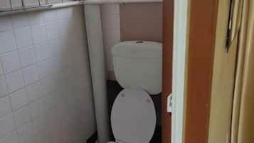 A small bathroom with a toilet, a white tiled wall, and a beige door.