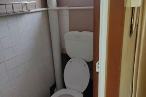 A small bathroom with a toilet, a white tiled wall, and a beige door. - Marina Hotel Kemaman (Chukai)