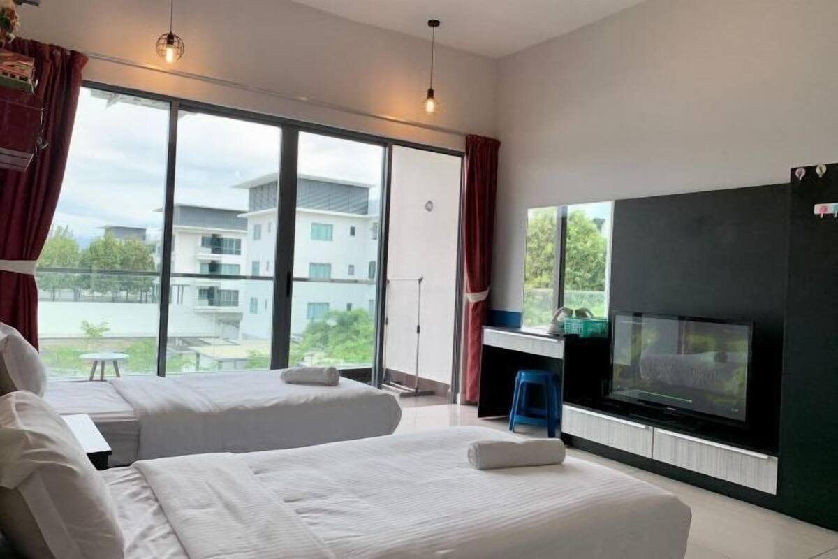 A hotel room with two beds, a TV, and a large window offering a view of buildings and greenery.