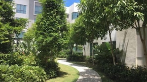 A pathway curving through a lush garden with tall trees and dense foliage, leading to a modern building with large windows. - Paradise Suite at the Loft, Imago (Kota Kinabalu)