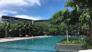 A swimming pool with clear blue water, surrounded by palm trees and a building with balconies. - Paradise Suite at the Loft, Imago (Kota Kinabalu)