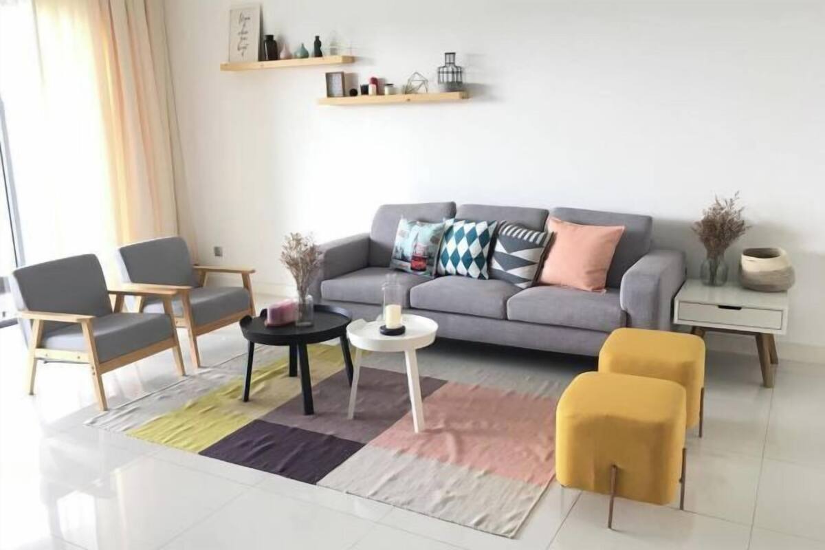 A modern living room with a grey sofa, two armchairs, a coffee table, and a yellow ottoman.