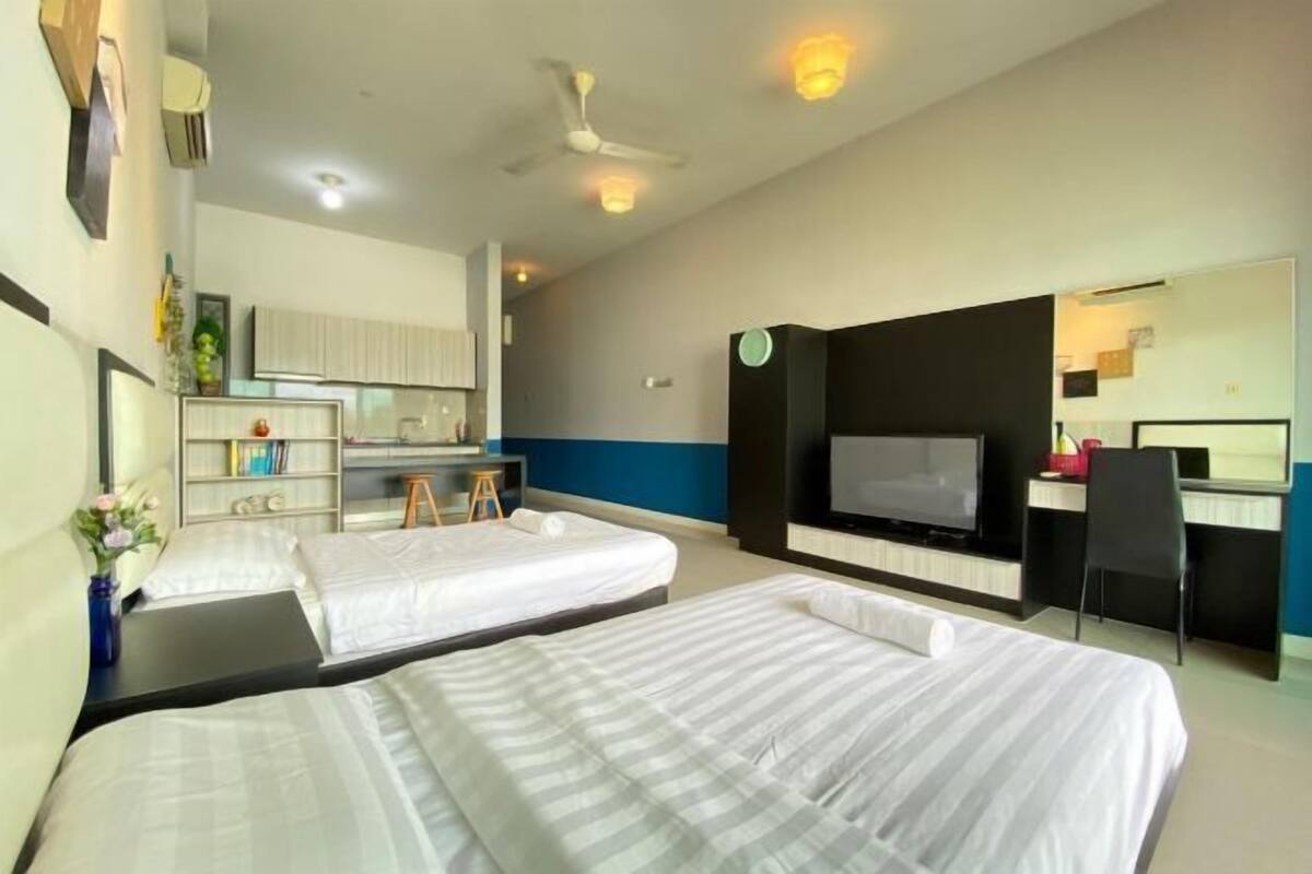 A hotel room with two beds, a desk, a TV, and a kitchenette.