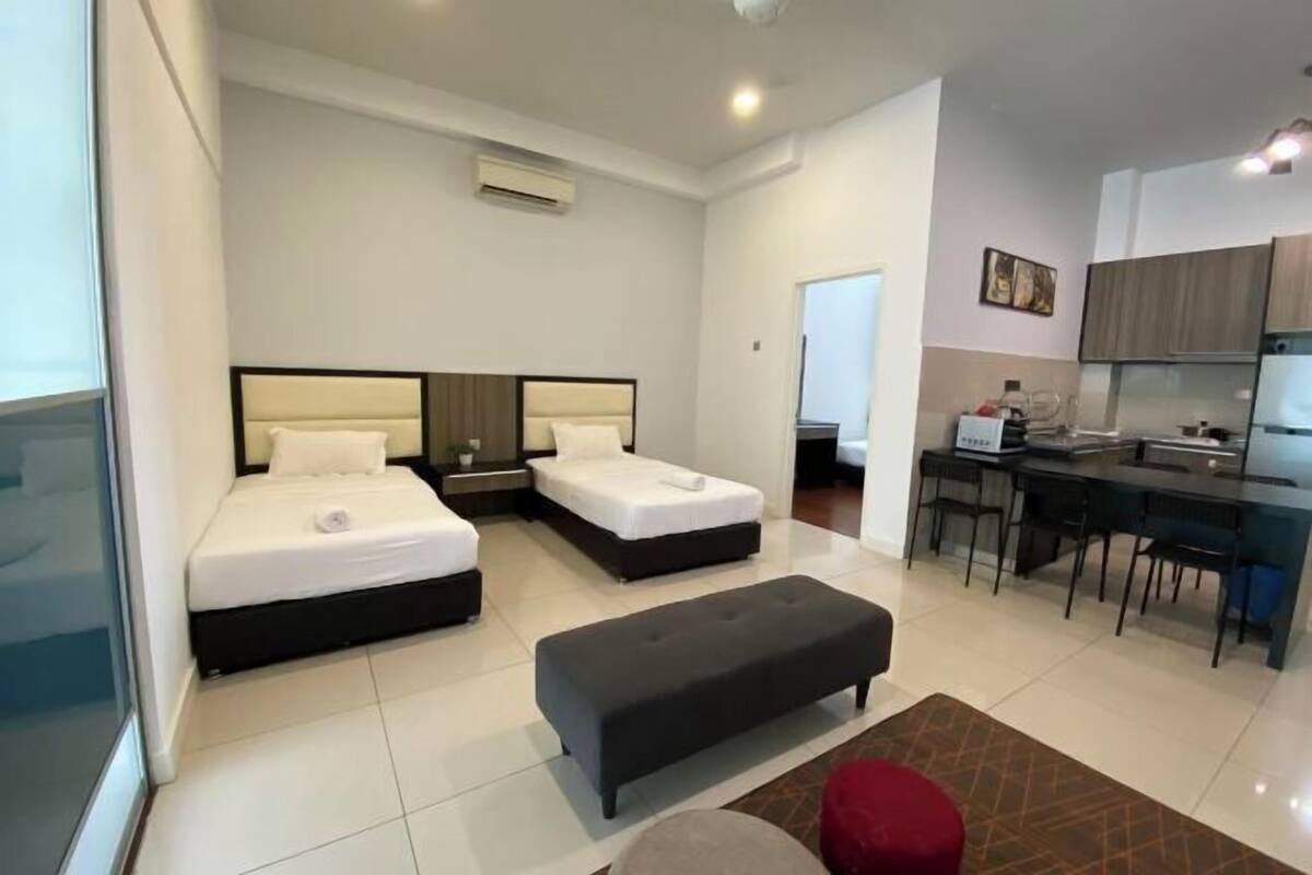 A modern hotel room with two beds, a kitchenette, and a seating area.