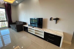 Una sala de estar moderna con televisor de pantalla plana, un sofá, una mesa consola de mármol y un ventanal con cortinas.