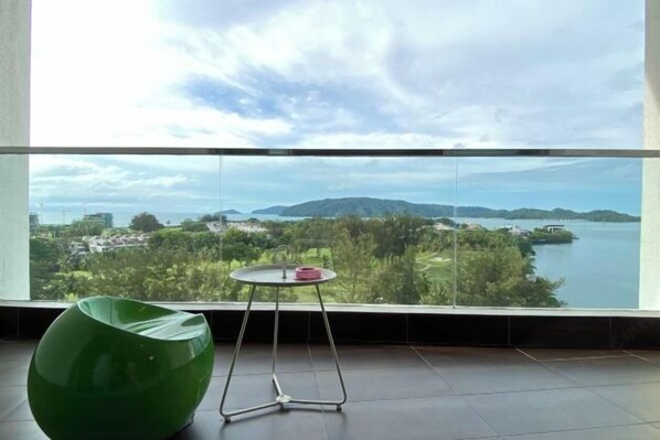 A room with a large window, a green chair, and a small table with a red object. - Paradise Suite at the Loft, Imago (Kota Kinabalu)