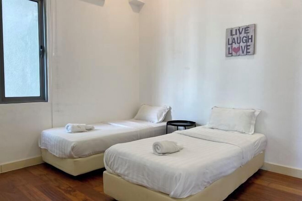 Una habitación con dos camas individuales, una mesita, una ventana y un letrero en la pared que dice 'LIVE LAUGH LOVE'.