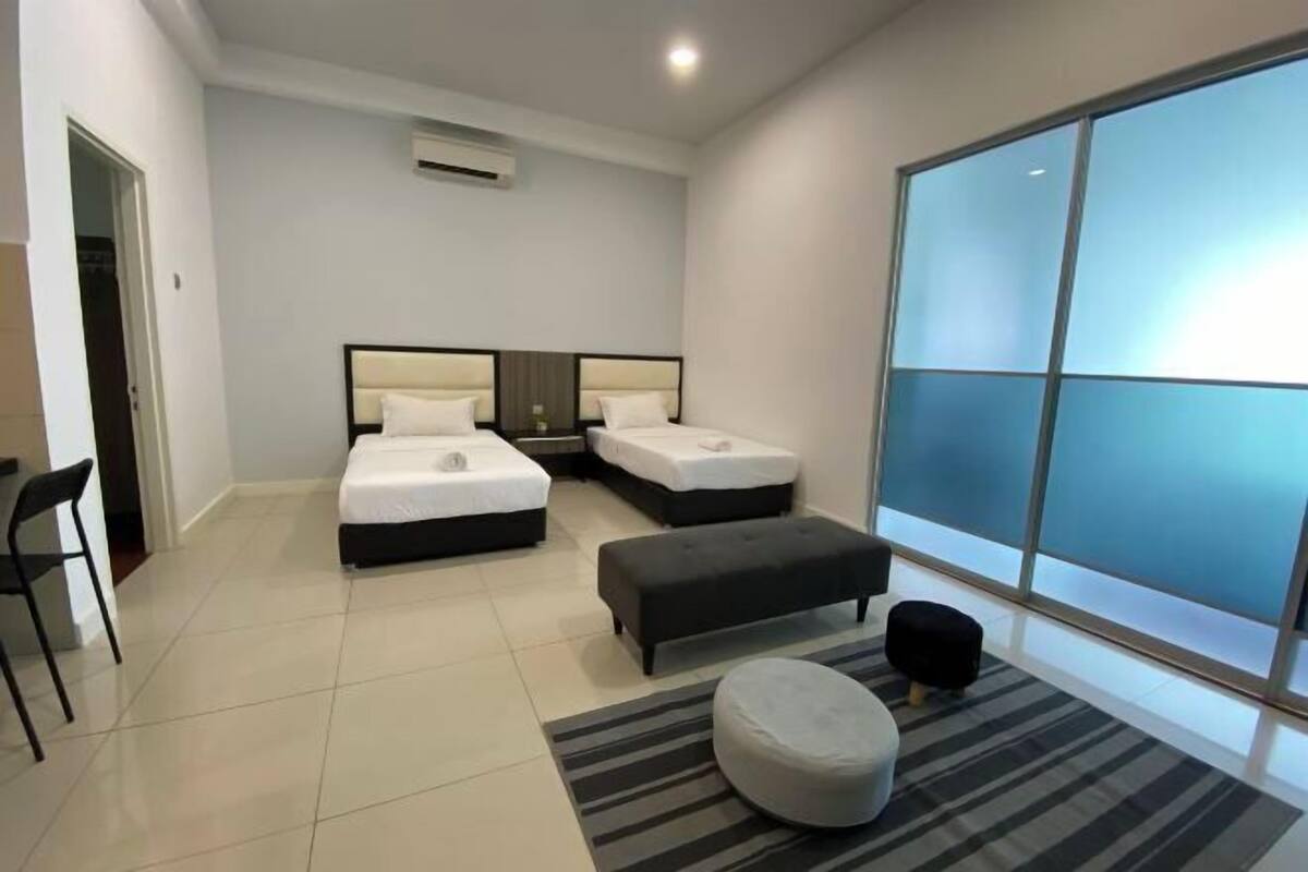A hotel room with two beds, a desk, a chair, a large window, and a sliding door.