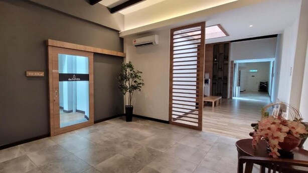 A modern hotel lobby with a wooden reception desk, a glass door leading to a waiting area, a potted plant, and a decorative plant arrangement. - The Nines Hotel Melaka (Malacca City)