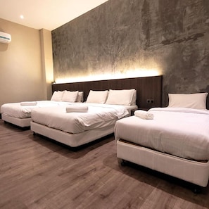 Ein Hotelzimmer mit drei Betten, einer Wand aus Betonoptik und Holzboden.