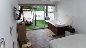 Ett modernt sovrum med en stor säng, en inbyggd TV, ett badrum med badkar och en skjutdörr i glas som leder ut till en uteplats.