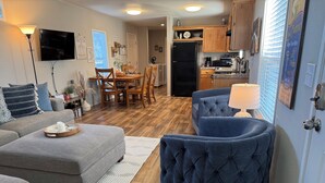 A modern living room with a grey sofa, a blue armchair, and a dining area with wooden chairs and a table.