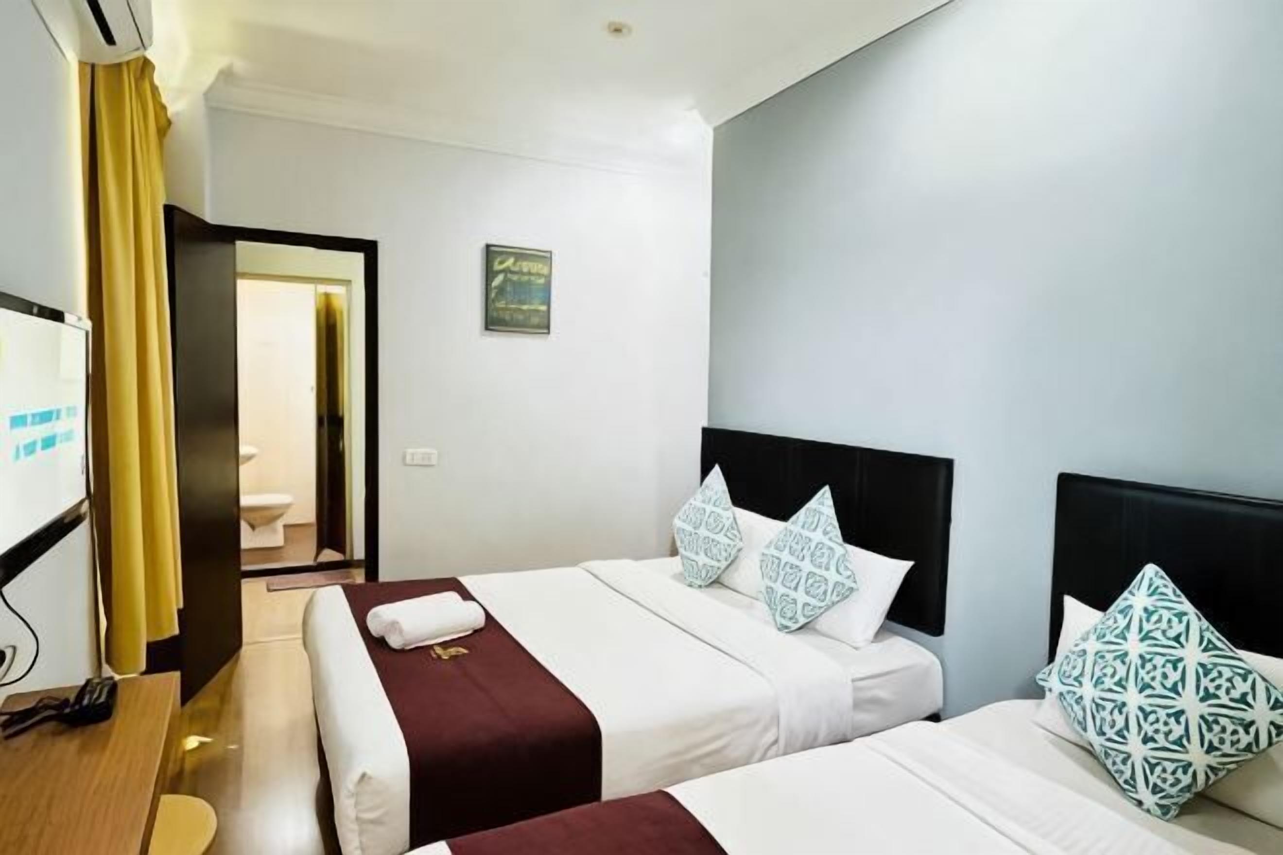 A hotel room with two beds, a desk, and a bathroom visible through an open door.
