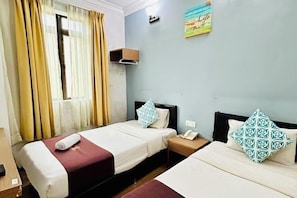 A hotel room with two single beds, a nightstand with a phone, and a window with curtains.