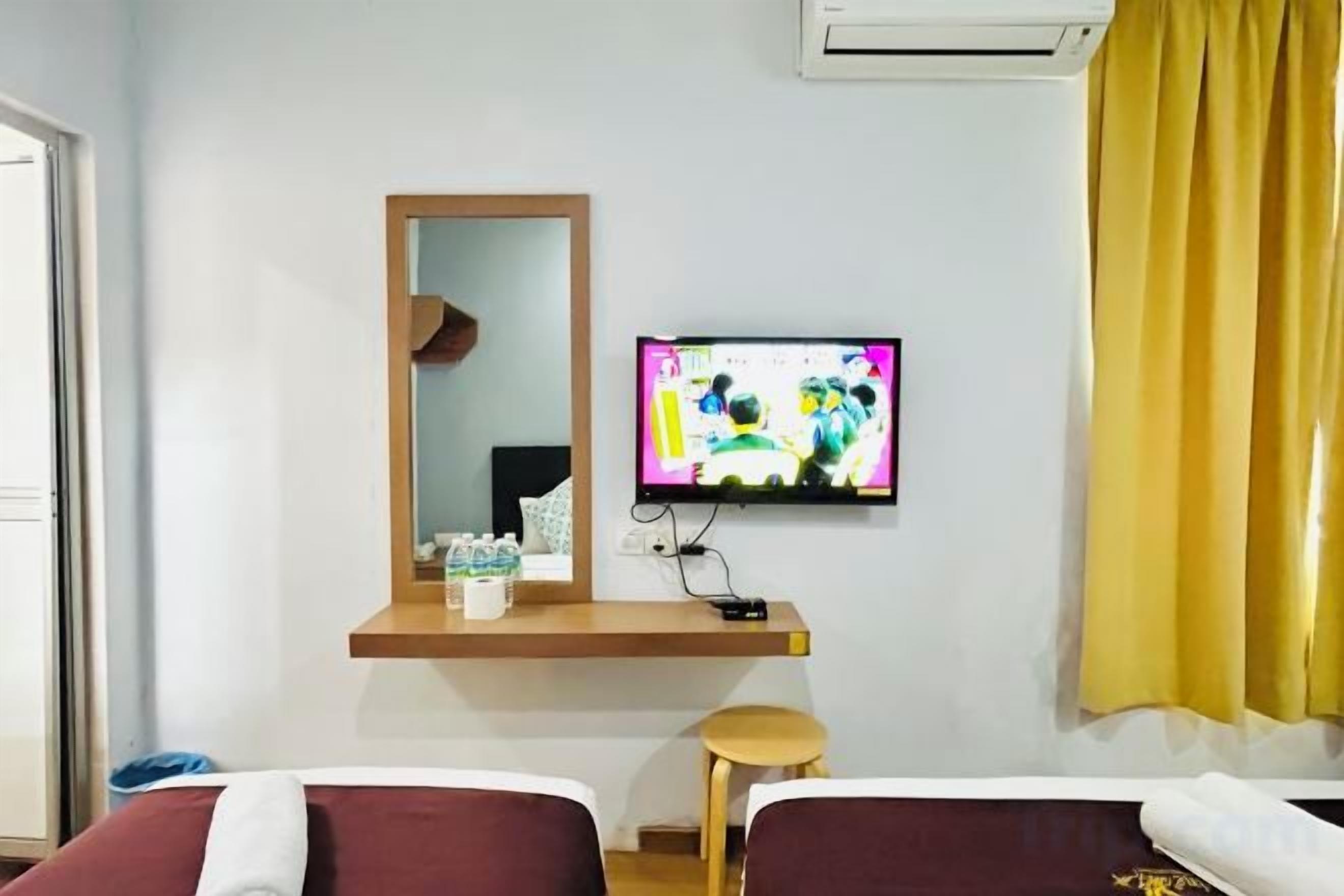 Quarto de hotel com cama, televisão na parede, espelho e janela com cortinas amarelas.