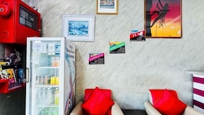 A room with a refrigerator, a sofa with red cushions, and a wall with framed pictures and small signs. - Charisma Hotel (Kuala Kuantan)