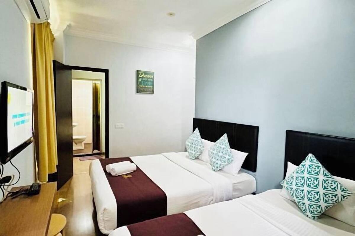 A hotel room with two beds, a TV, a desk, and a bathroom visible through an open door.