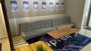 A modern hotel room with a grey sofa, a wooden coffee table, and a colorful rug with the word "PIRU" on it. - Terminal VIP Lounge @ Near KLIA Sepang (Sepang)
