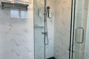 Box doccia in vetro con soffione a mano, portasci e porta in vetro con maniglia in metallo.