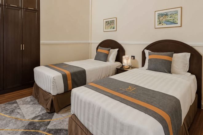 Two single beds with matching headboards and footboards, a wooden wardrobe, and a nightstand with a lamp.