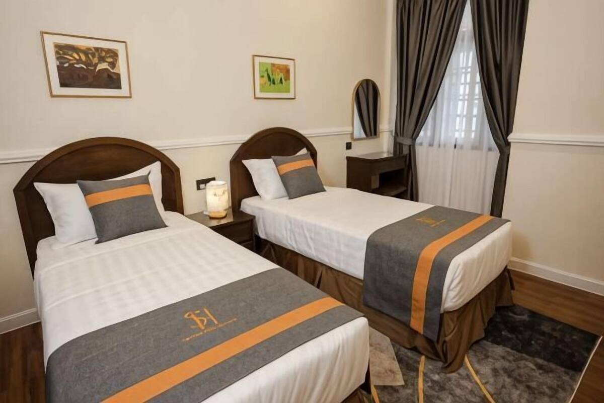 Two single beds with matching headboards and footboards, a bedside table with a lamp, and a window with curtains.