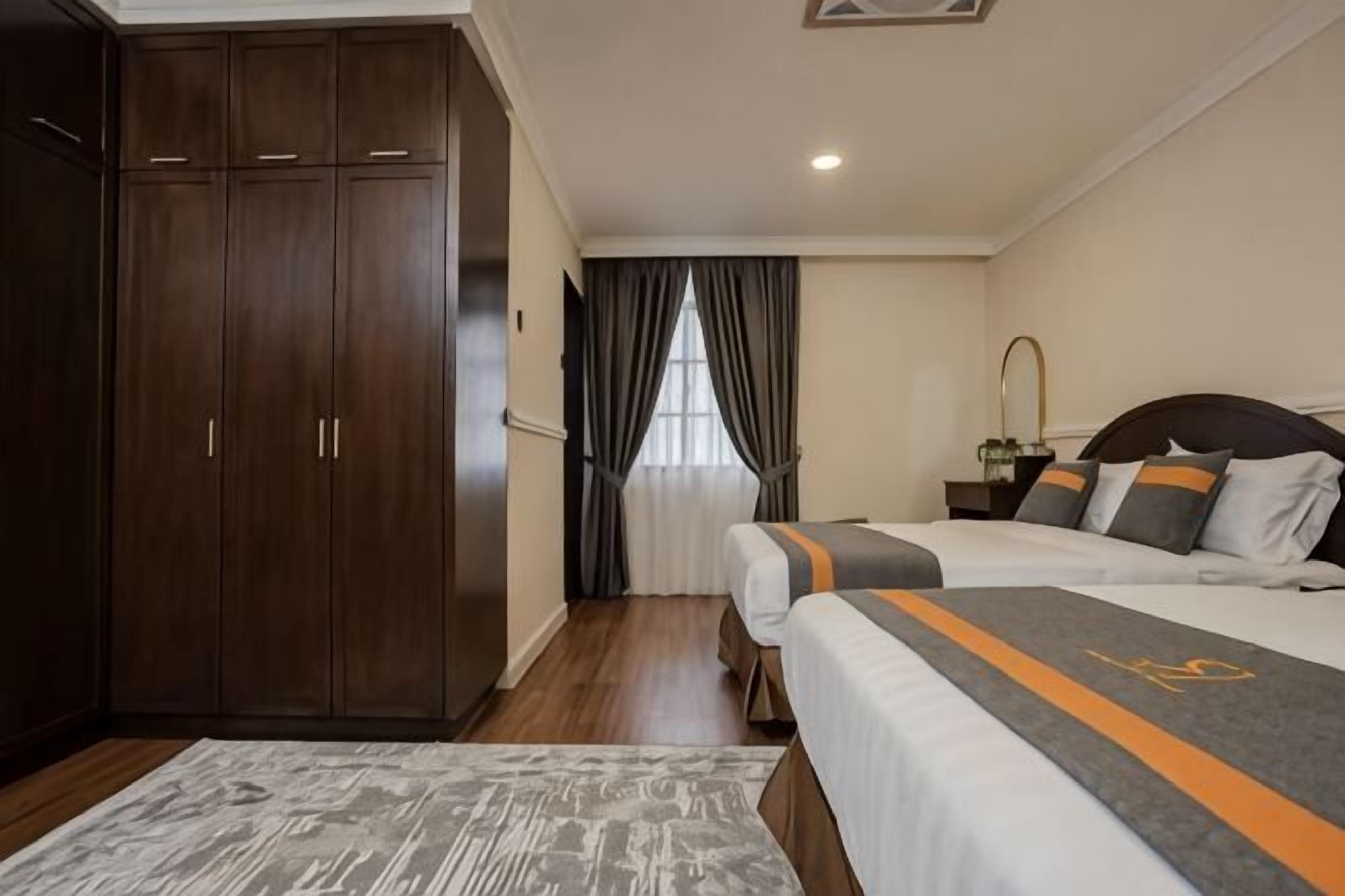 Habitación de hotel con armario, cama con colcha a rayas, mesita de noche y ventana con cortinas.