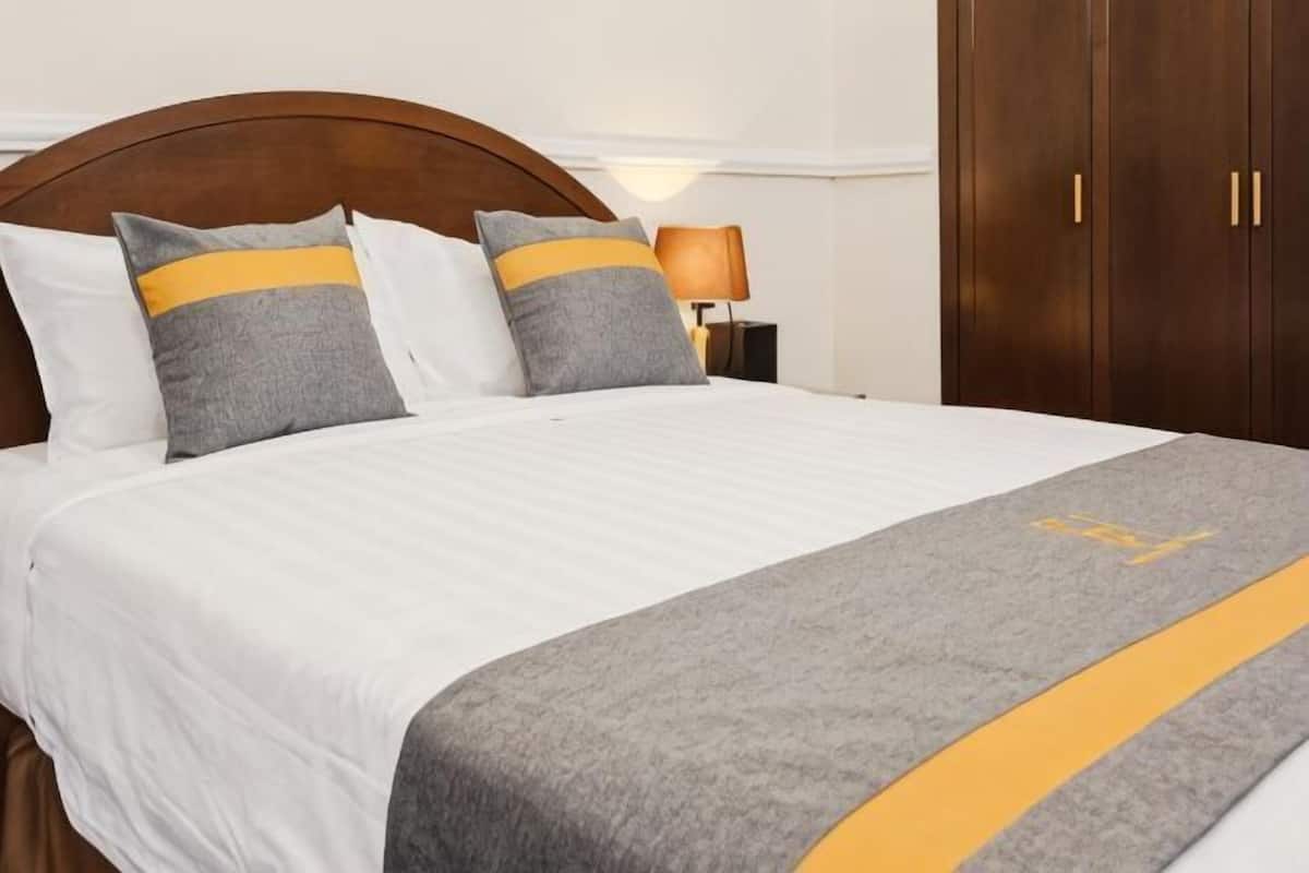 A neatly made bed with a grey and yellow bedspread, a wooden headboard, and a nightstand with a lamp.