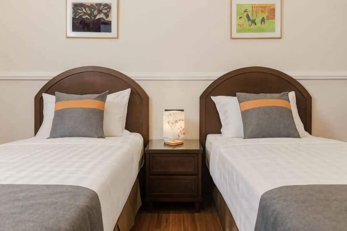 Two twin beds with headboards, a bedside table with a lamp, and artwork on the walls.