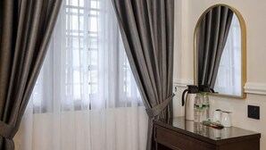 A hotel room with a bed, a bedside table with a bottle and glasses, a mirror, and curtains. - SpringHill Resort (Brinchang)