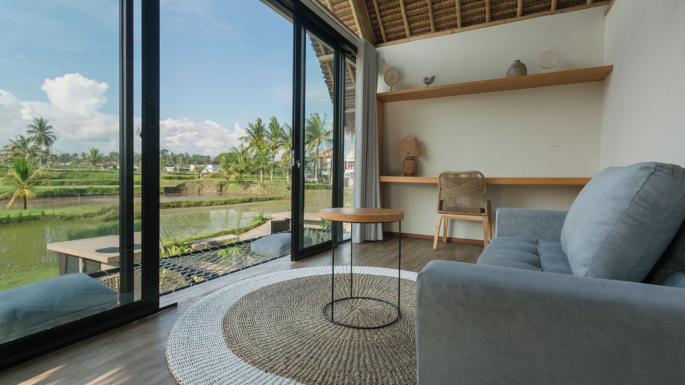 Un salon moderne avec une grande fenêtre, un canapé gris, une table basse ronde et un tapis tissé.