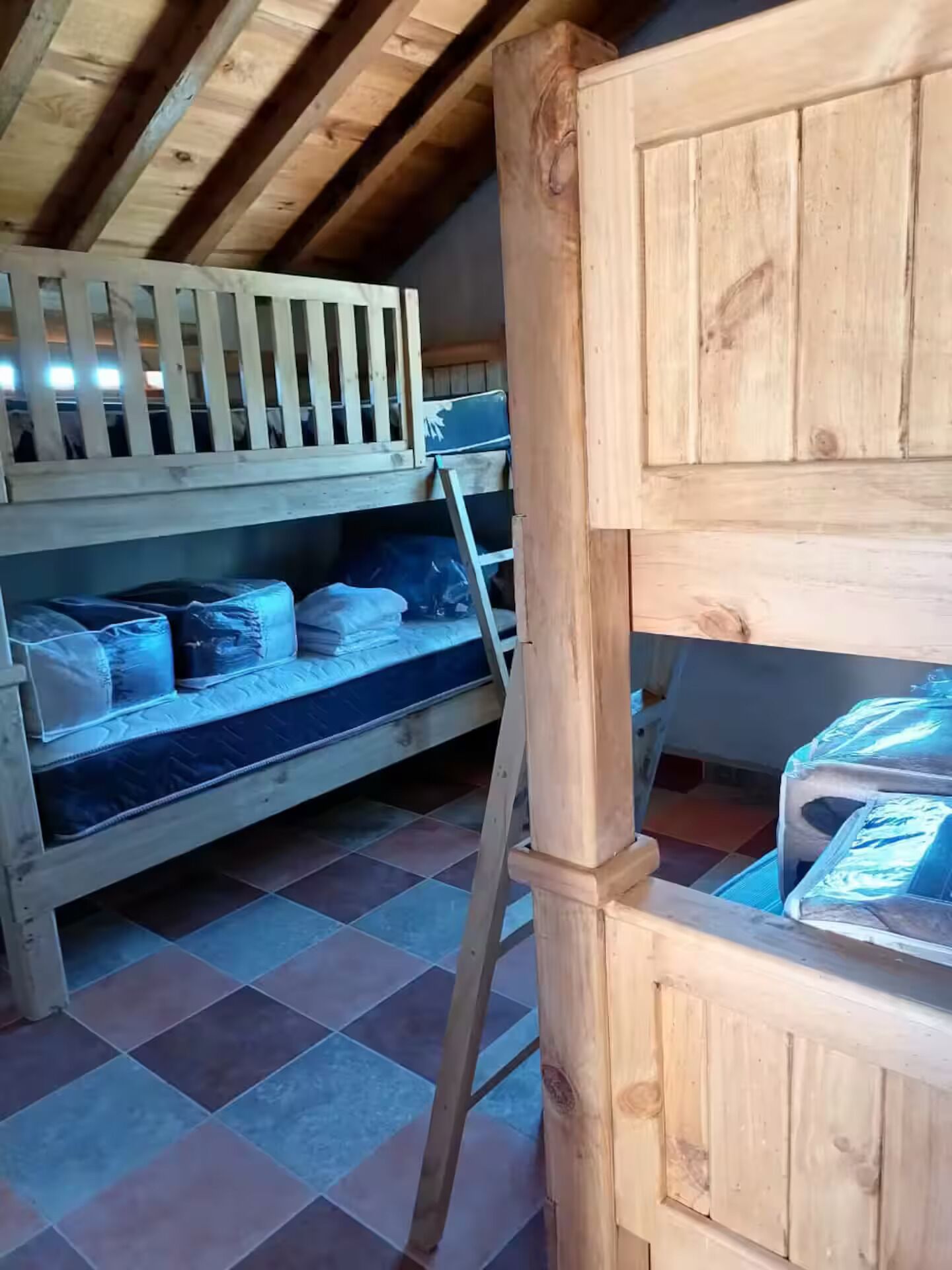 Habitación con literas de madera, una escalera y protectores para colchones.