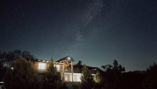 Une grande maison à deux étages, dotée d’un balcon, entourée d’arbres et baignée par la lumière d’un ciel étoilé.