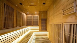 A sauna with wooden benches and a slatted floor, illuminated by overhead lights.