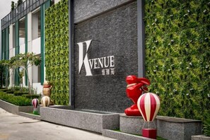 A building with a prominent 'KVENUE' sign, a red sculpture, and a green wall. - K Avenue by CAIRO (Donggongon)