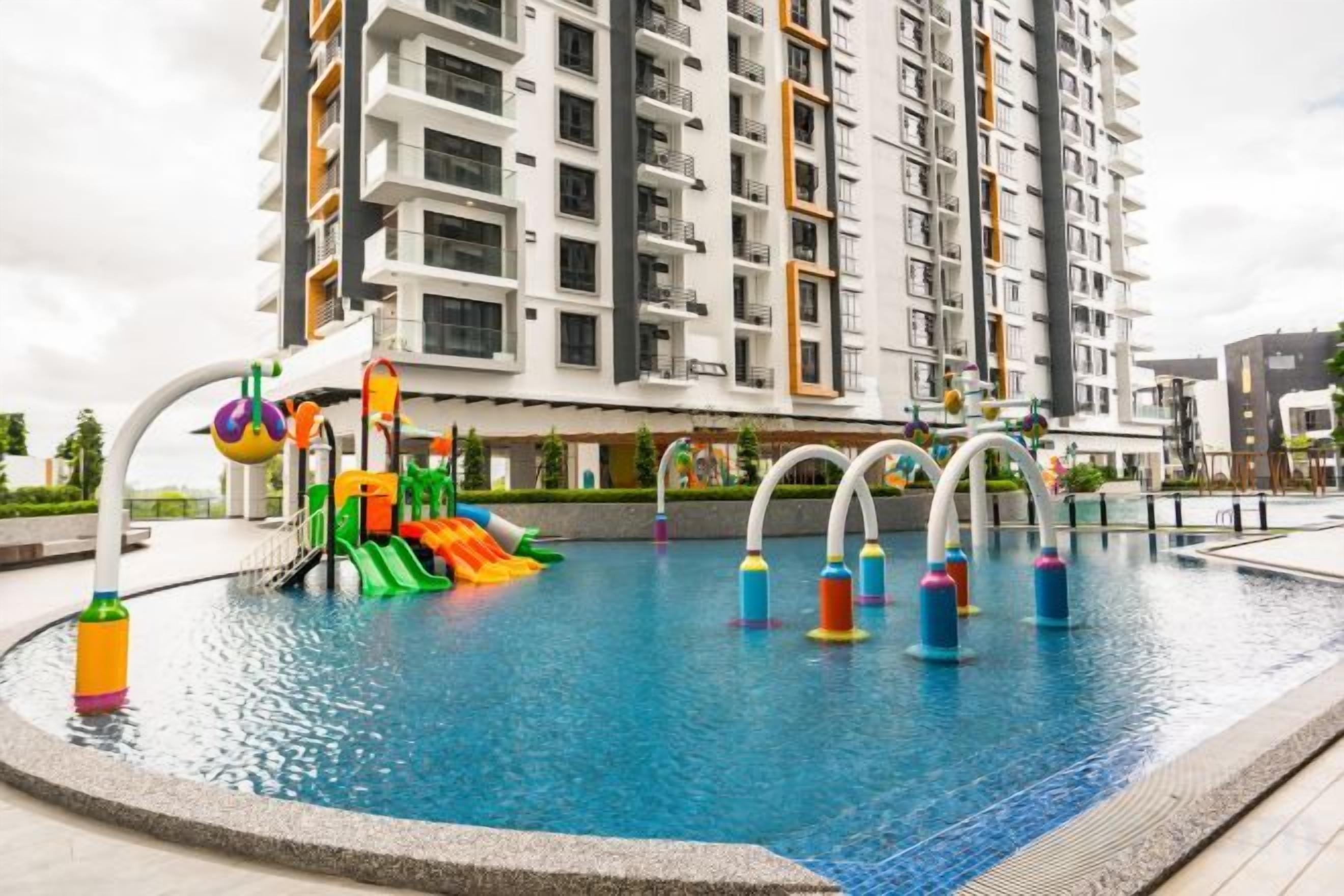 Una piscina con tobogán y múltiples chorros de agua, rodeada por un edificio residencial alto.