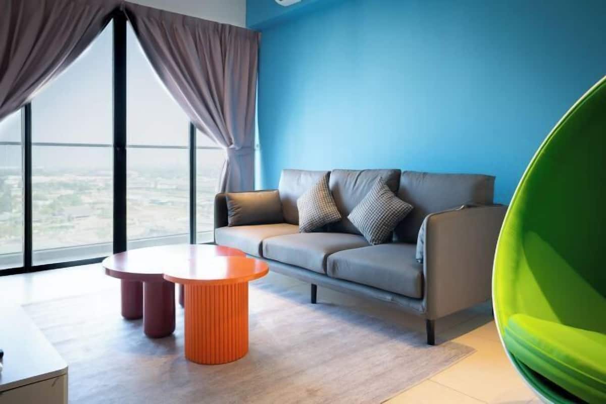 Un salon moderne avec un canapé, une table ronde orange et une vue dégagée grâce à de grandes fenêtres.