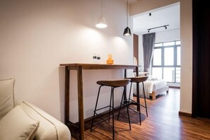 Une chambre moderne avec une table en bois, deux tabourets de bar, un canapé, un lit et une grande fenêtre.